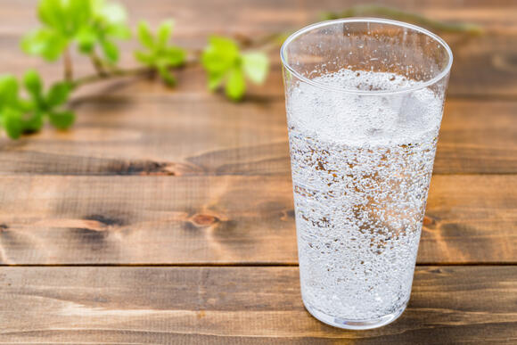 Glas klart vatten med synliga bubblor, äldre händer som håller glaset