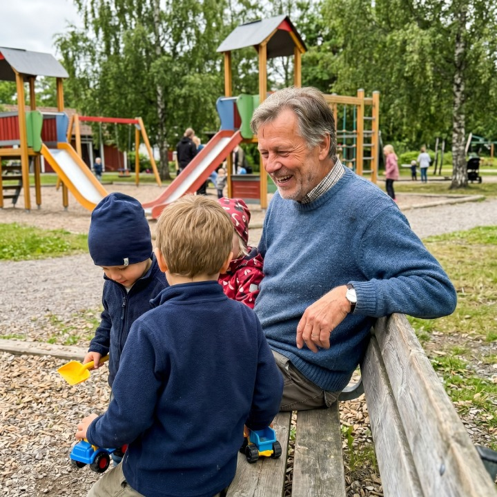 Kvinna i 60-årsåldern häller vatten från en modern flaska i ett ljust kök, morgonsol